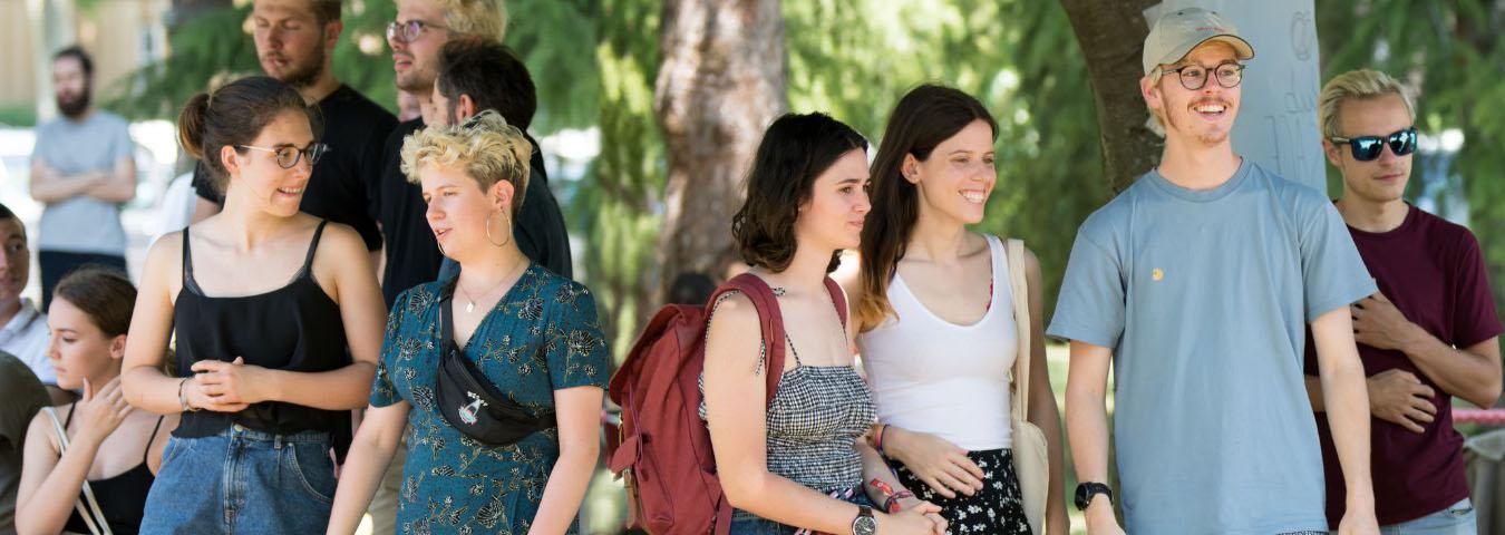 Photo d'étudiants et étudiantes de l'ENTPE, souriants, debout sous des arbres, en train de discuter 