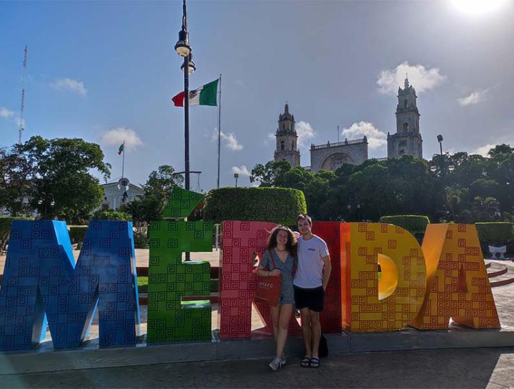 Une femme et un homme devant enseigne de la ville Merida au Mexique